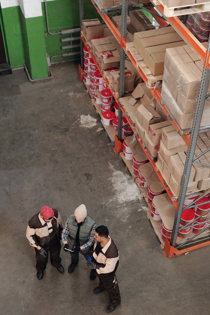 Group of warehouse workers discussing logistics and inventory in a large storage area with shelves and packages.